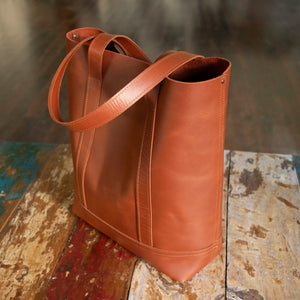 The Tan Everyday Leather Tote sitting on a distressed vintage wooden table.