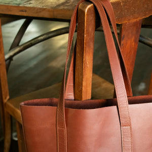 A close up of the Tan Everyday Leather Tote hanging off the back of a wooden chair.