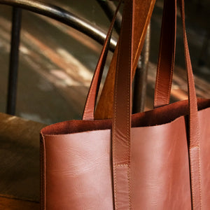 A close up of the Tan Everyday Leather Tote hanging off the back of a wooden chair.