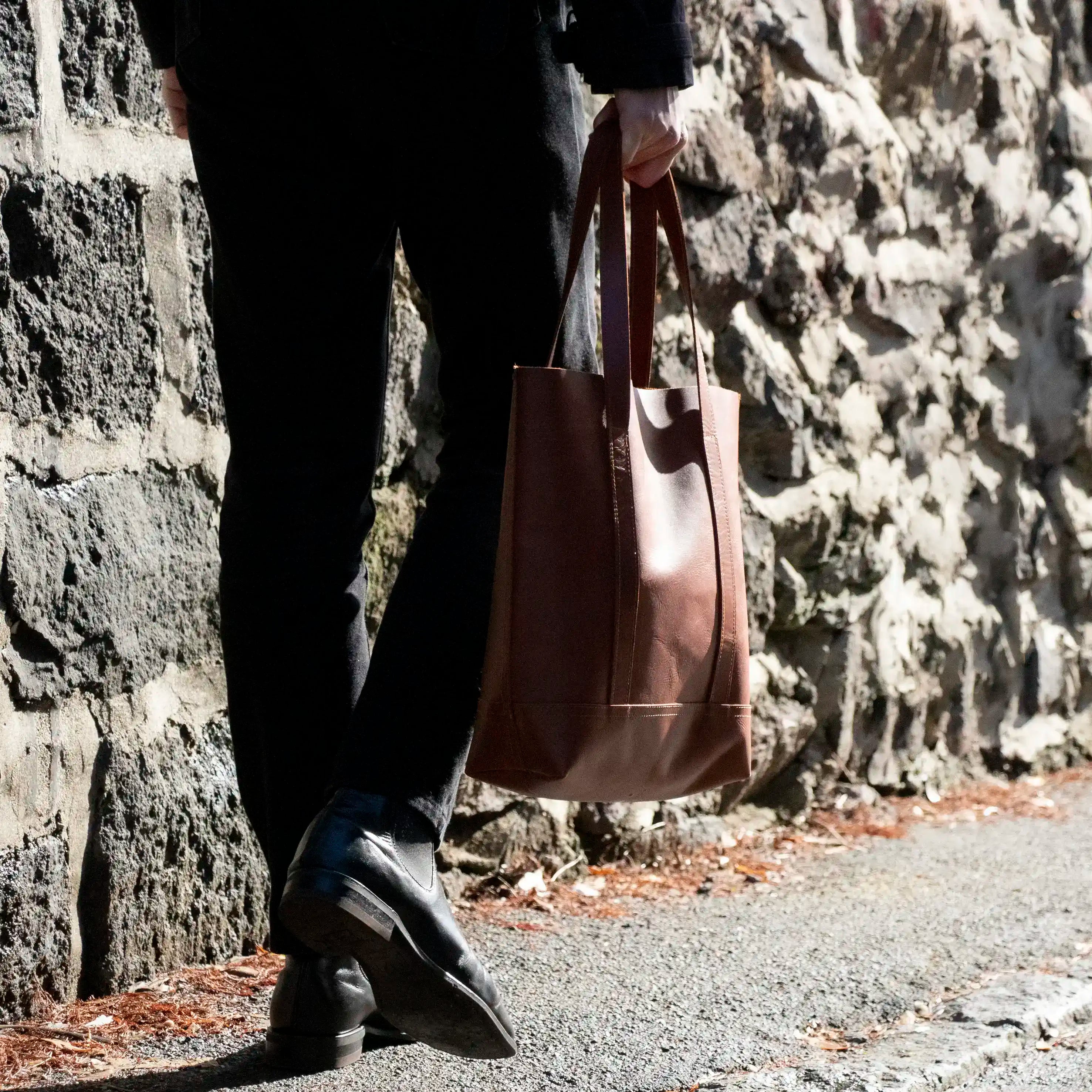 A close up of a Man walking away in the sun with the Tan Everyday Leather Tote.