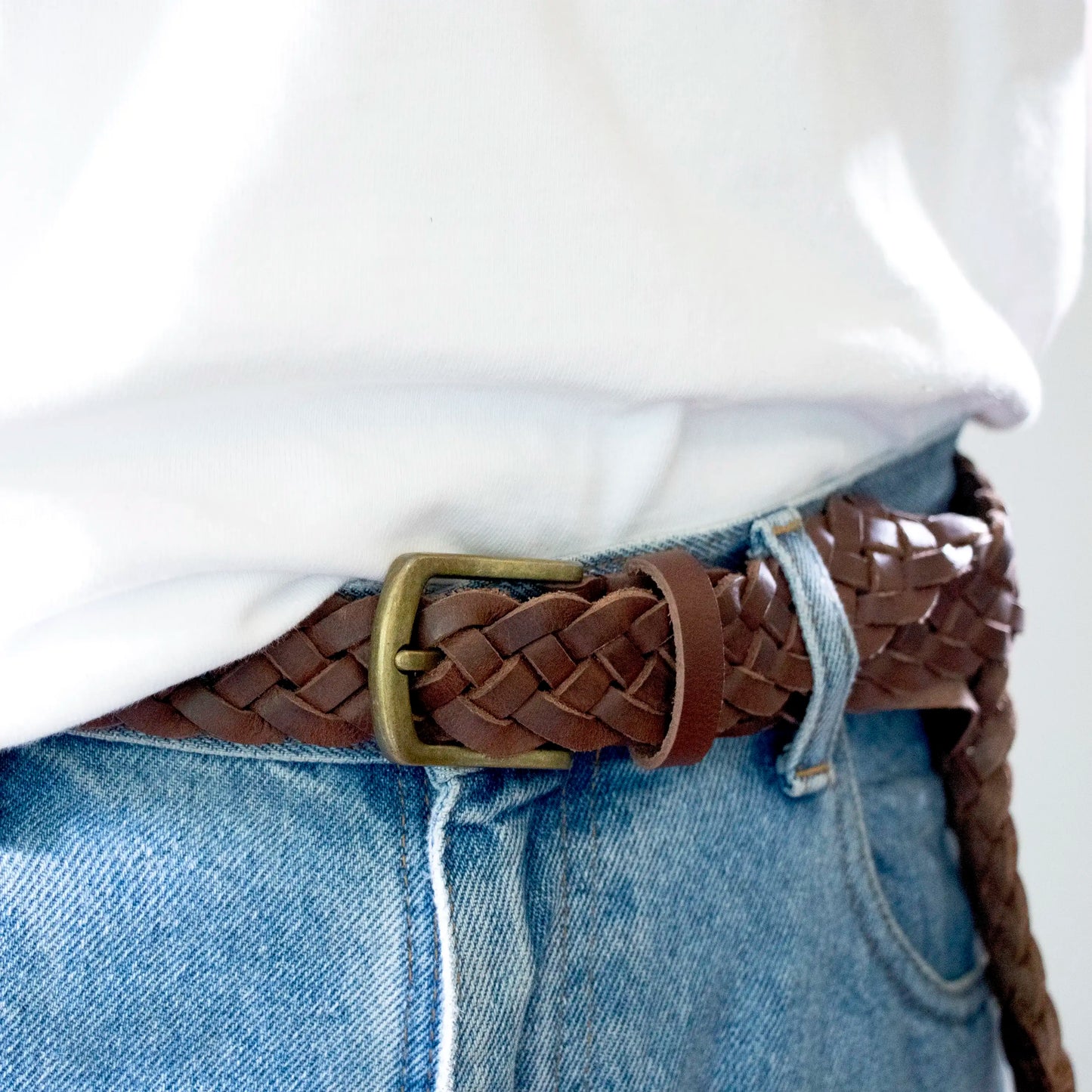 A close up of the Brown Hand-Woven Leather Belt with a Brass Buckle, worn with blue jeans and a white t-shirt.