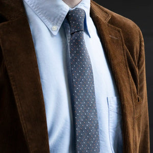 A close up of the Denim White Rust Pin Dot Tie worn with a blue button down shirt and a brown corduroy jacket 