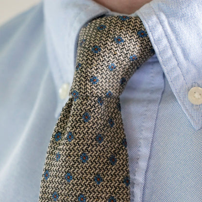 A close up of the Hessian Texture with Blue Flower Tie worn with a Soft Blue Button Down Shirt. 