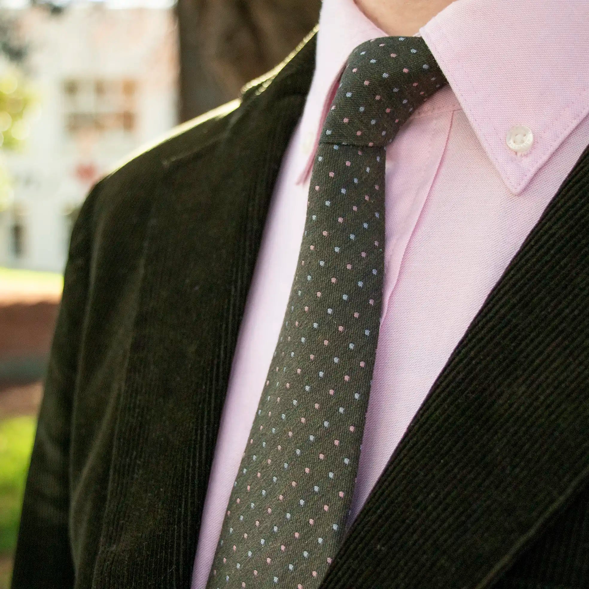 The Olive Sky Pink Pin Dot Tie worn outdoors with a Soft Pink Button Down Shirt and a Forest Green Corduroy Blazer. 